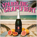 Bottle of sparkling grapefruit wine with pink grapefruits on a beach setting